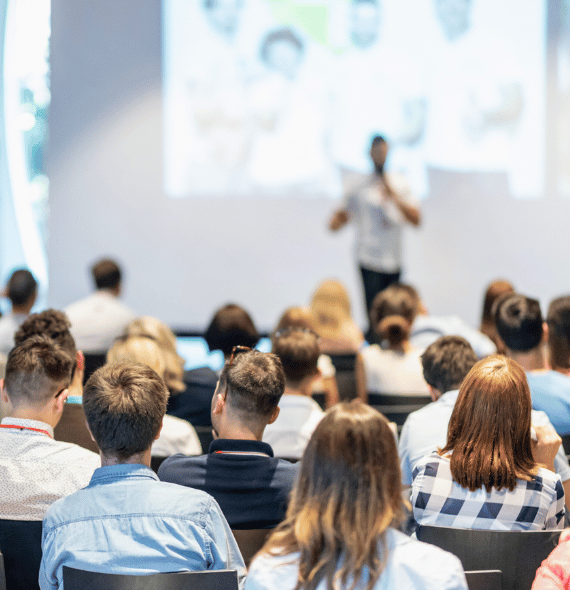 Presenter at a conference with audience members in the foreground