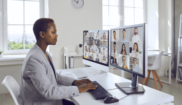 Professional woman sitting at a desk with two monitors attending a virtual meeting
